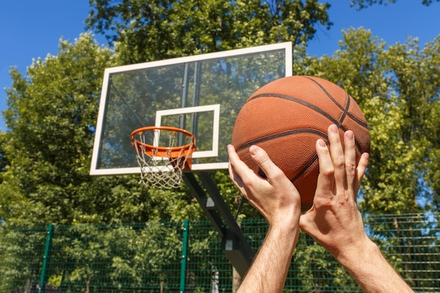 Крупным планом мужские руки бросают баскетбольный мяч в мишень на открытом воздухе