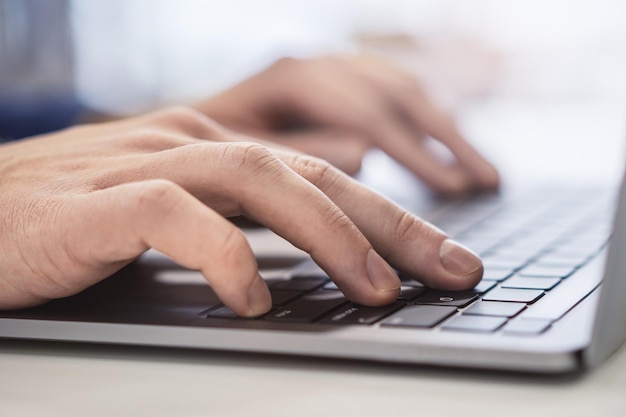 Closeup of male hands typing on modern laptop keyboard on blur office background