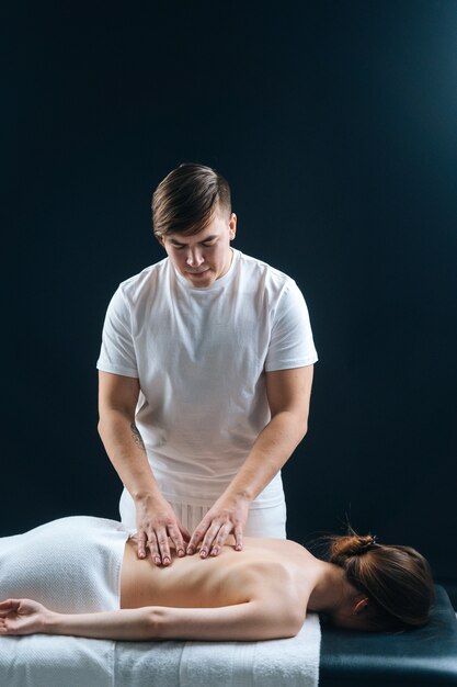 Closeup of male masseur massaging small of back of young woman lying on massage table