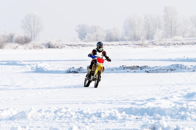 クローズアップ男性バイカーは、冬のモトクロスカップ中に雪の丘でバイクに乗ります 極端なバイカーは、冬のオフロードバイクで雪の中を乗ります 冬の極端なエンターテイメント