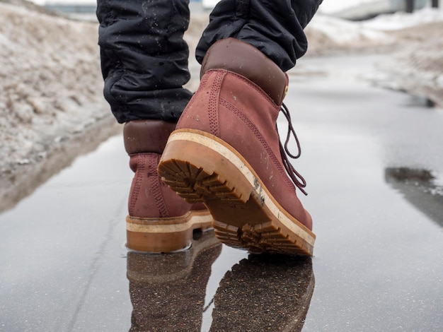 Closeup of a man in brown shoes walking on wet asphalt in spring Snow all around the road