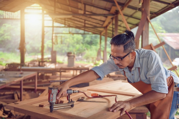 Closeup of a man carpenter using a nail gun.Carpenter using air nail gun doing wooden furniture work,vintage style