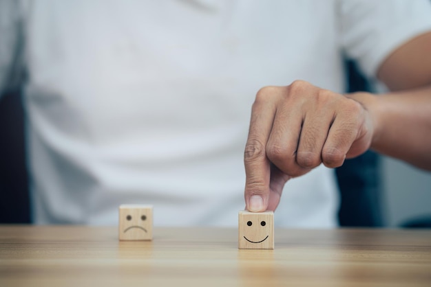 Closeup man choose smiley face and blurred sad face icon on\
wood cube