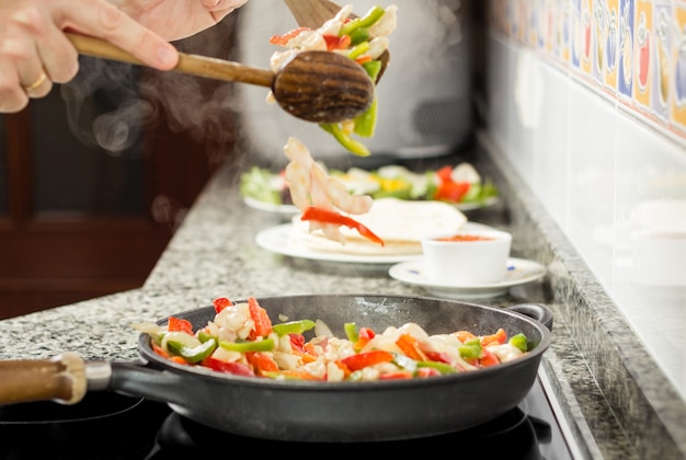 黒い鍋でメキシコ料理のために野菜と鶏肉を調理する男のクローズアップ