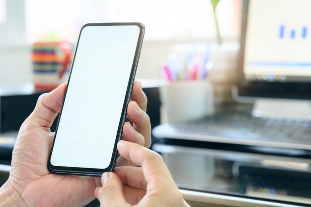 Closeup man hand holding smartphone with blank white screen while working at office desk, blank screen