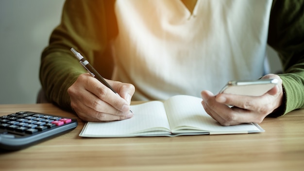 Closeup man hand using smart phone and write a book