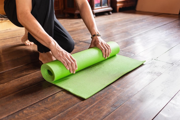 Closeup of man handrolling a green yoga mat at home healthy\
life and healthy living concept