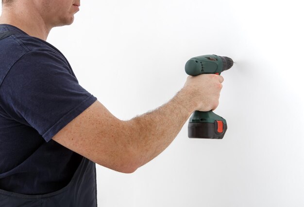 Closeup of a man holding a cordless screwdriver drill makes a hole in the wall