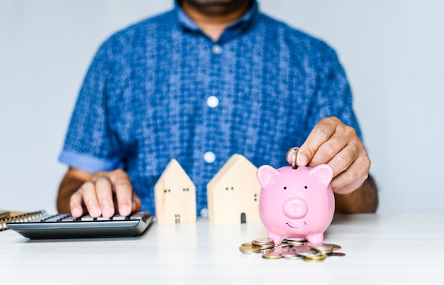 Closeup man holding a pink pig piggy bank and collecting coins in a piggy bank Concept of men collects money for a home and car payment during COVID or coronavirus outbreak Blurred white background