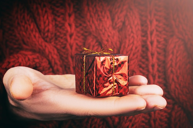 Крупный план человека, держащего в руке маленький красный рождественский подарок