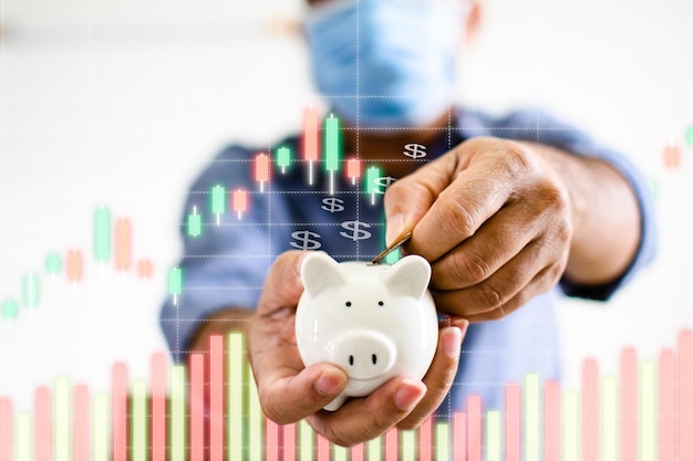 Closeup man holding a white pig piggy bank and collecting coins in the piggy bank Concept of men wearing a face mask to collect money during COVID19 or coronavirus outbreak Blurred white background