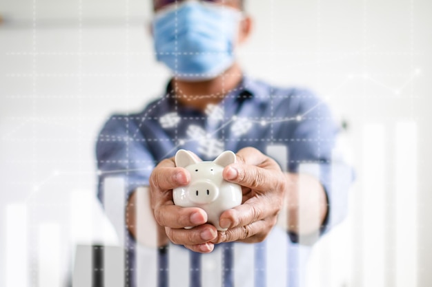 Closeup man holding a white pig piggy bank Concept of men wearing a face mask to collect money during COVID19 or coronavirus outbreak and investment budget wealth business Blurred white background