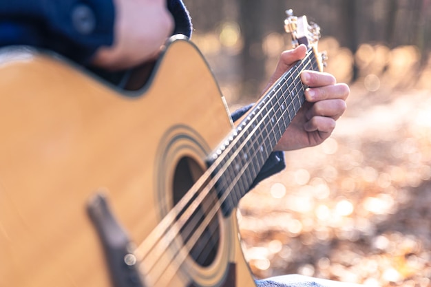 Closeup a man plays an acoustic guitar in the autumn forest