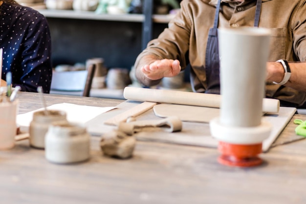 A closeup of a man potter rolls a brown clay rolling pin on a special fabric on a wooden table to make a plate Horizontal photo