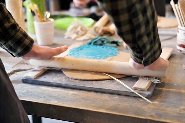 A close-up of a woman potter rolls a brown clay rolling pin on a