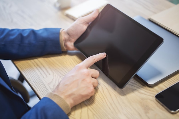 Closeup of a man's finger making contact with a stateoftheart tablet screen device resting on a desk against the indistinct buzz of a light office environment