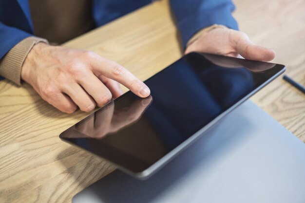 Foto primo piano del dito di un uomo che entra in contatto con uno schermo tablet all'avanguardia appoggiato su una scrivania contro il ronzio indistinto di un ambiente di ufficio luminoso