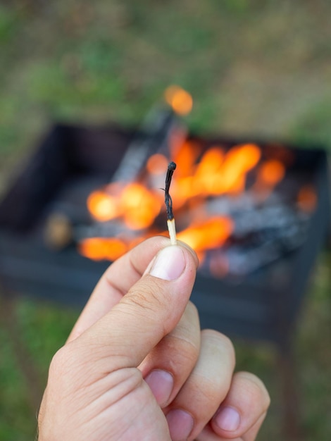 Foto primo piano della mano di un uomo in possesso di un fiammifero bruciato un fuoco sta bruciando in background messa a fuoco selettiva