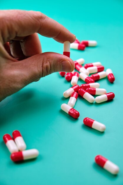 Близкий снимок руки мужчины, держащей красно-белую капсулу на зеленом столе с множеством таблеток