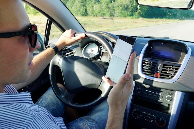 Closeup of a man's hand holding a smartphone Businessman texting while sitting in a car Holding a steering wheel and using a mobile phone