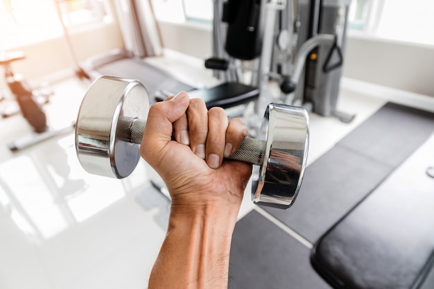 Крупный план рука человека держит гантель с его левой рукой в спортзале, концепцией для тренировки и здравоохранением.