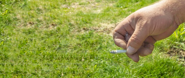 Closeup of a man's hand smoking a cigarette on a grass background outdoors smoking cessation concept space for text on the left