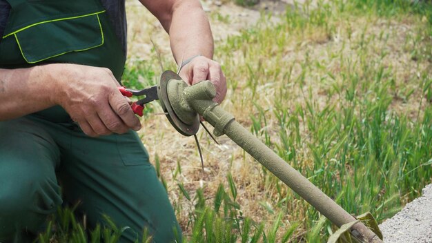 部品を交換するために芝刈り機を分解する男性の手のクローズアップ 部品を交換して除草機を維持および修理する