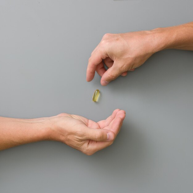 Closeup of man\'s hand throwing a capsule with fish oil on grey\
background sport healthy lifestyle medicine nutritional supplements\
and people concept