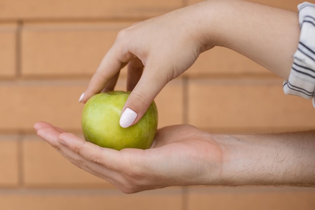 Closeup of a man's palm with a green apple on it while a woman's hand picks it up