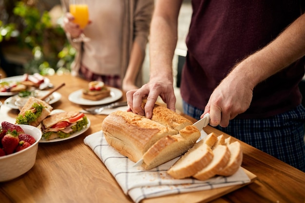 Closeup of man slicing bread at dining table