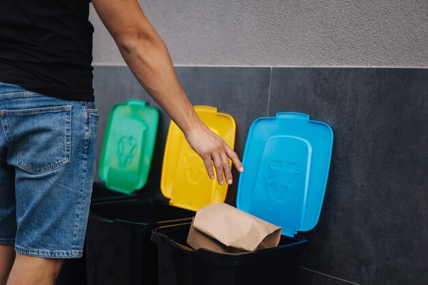 Closeup of man throwing peace of cardboard in recycling bins humen hand holding paper near the