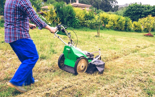 closeup of man with straw hat and plaid shirt mowing lawn with a lawnmower machine