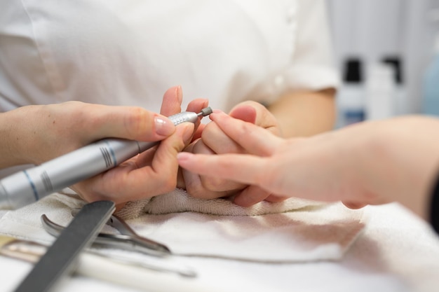 Closeup of manicurist doing hardware manicure to a young beautiful girl in the spa salon