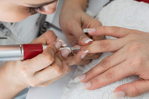 Closeup of a manicurist polishing nails made of polygel with an electric nail buffer