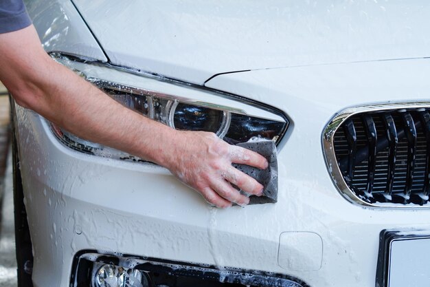 Foto la mano di un uomo in primo piano sta lavando un'auto. la mano tiene una spugna per lavare l'auto. pulisce l'automobile con una spugna.