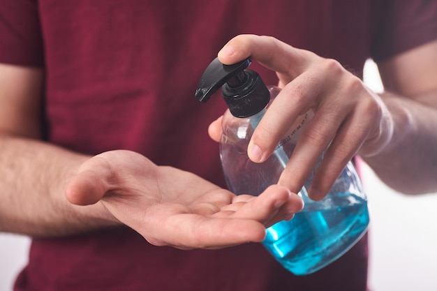 Closeup mans hand using antibacterial liquid soap to protect against COVID-19. Man uses gel for cleaning hands on a blue. Antiseptic, empty.