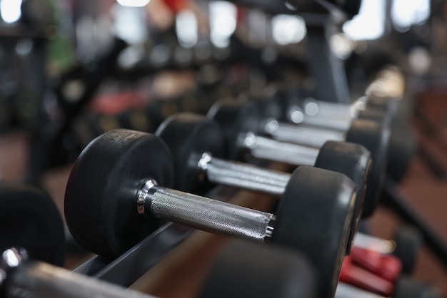 Primo piano di molti manubri neri su rack in palestra che modellano il corpo attraverso un regolare allenamento sportivo