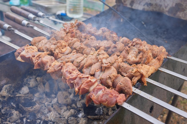Closeup of marinated big turkey or chicken meat steak shashlik or shish kebab preparing cooking on barbecue brazier grill over charcoal on burning coal Skewered roasted kebabs on BBQ grill
