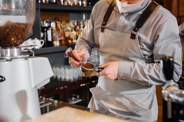 Primo piano di un barista mascherato che prepara un delizioso caffè al bar in una caffetteria