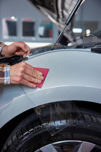 Closeup master hand with rubber scraper applying sticking protective film on car at vehicle workshop service station