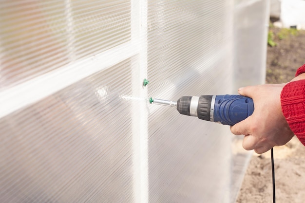 Closeup the master tightens the screw into the bar of the greenhouse to secure the polycarbonate