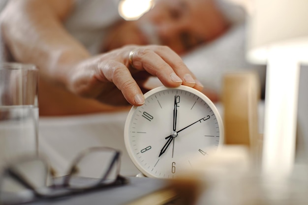 Closeup of mature man turning off alarm clock at bedside table