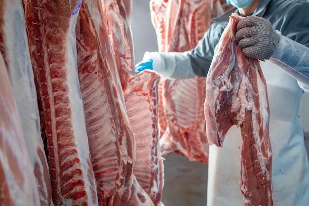 식품 산업에서 육류 가공의 근접 촬영 노동자는 냉장고에서 생 돼지 저장을 잘라냅니다