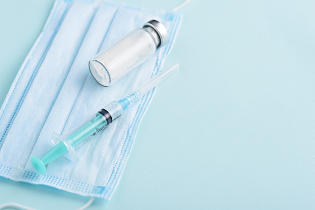 Closeup medical syringe, glass ampoule, medical mask on blue background, vaccination, inoculation concept, copy space