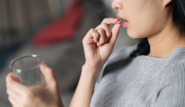 Closeup on medicine pill in hand of ill young woman laying on sofa at home