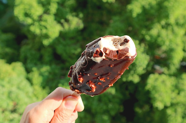 晴れた日に手に溶けるチョコレートに浸したアイスクリームバーをクローズアップ