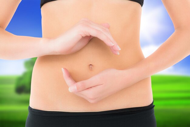 Closeup mid section of a fit woman with hand gestures against sunny green landscape