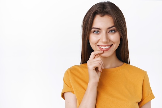 Closeup modern creative goodlooking female in yellow tshirt have inspiration to create something huge touching lip and smiling with pleased thoughtful expression white background