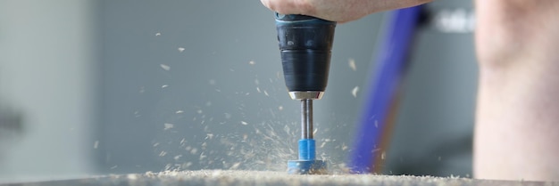 Closeup of modern electrical instrument drilling hole in wooden board sawdust on surface
