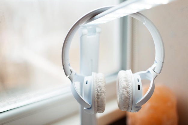 Closeup of modern wireless headphones hanging on room lamp